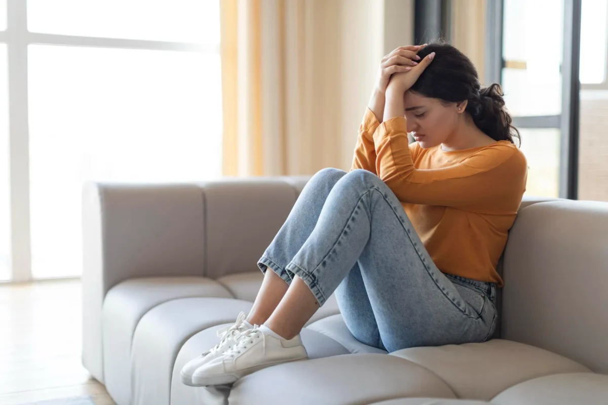 A woman sitting on the couch experiencing signs of emotional exhaustion from burnout